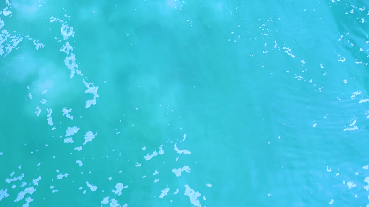 Bright aqua Los Cabos water fills the frame with white bubbles and faint darker bands visible below the surface, with no visible people.