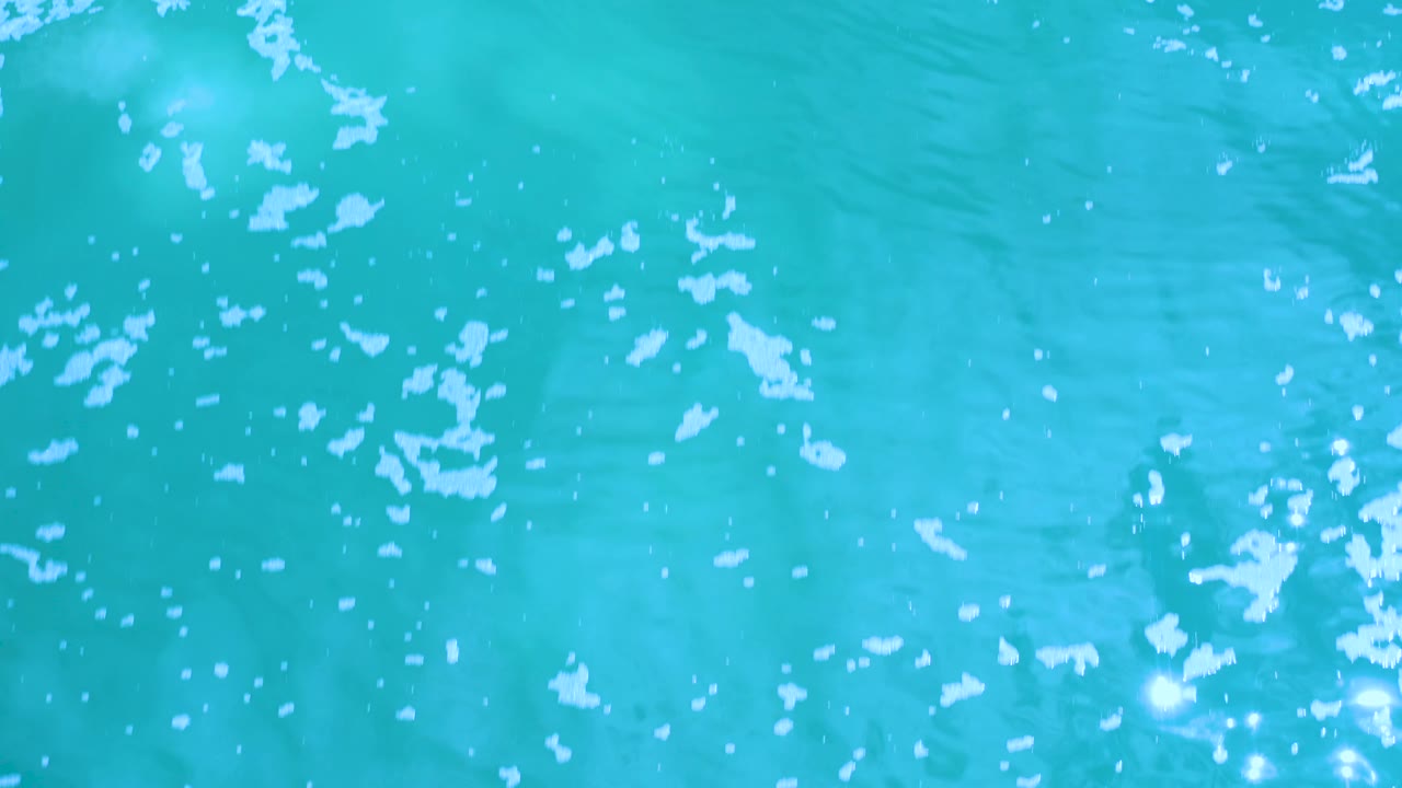 Turquoise Los Cabos water shows a denser scatter of white foam specks across the middle of the frame and no visible people.