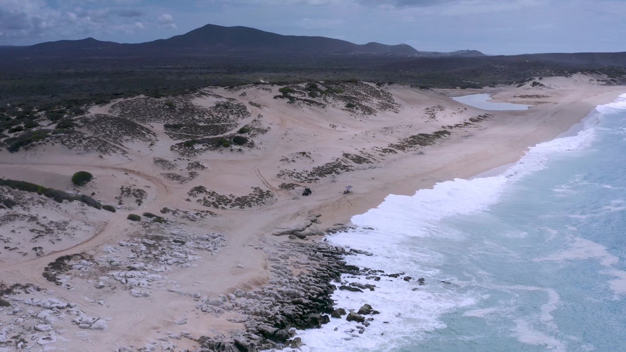 Aerial view of waves breaking beside sand dunes and rocky shore