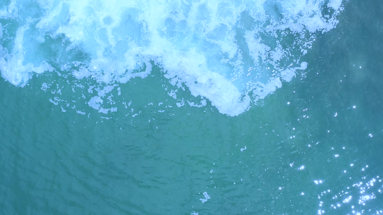 Top-down view of Los Cabos surf with a dense white foam patch across the upper left and blue-green open water below, with no visible people or structures.