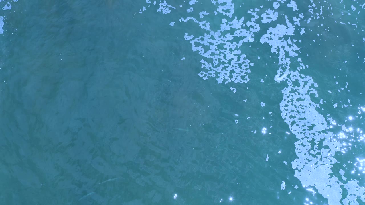 Top-down ocean surface with bright foam and light sparkles.