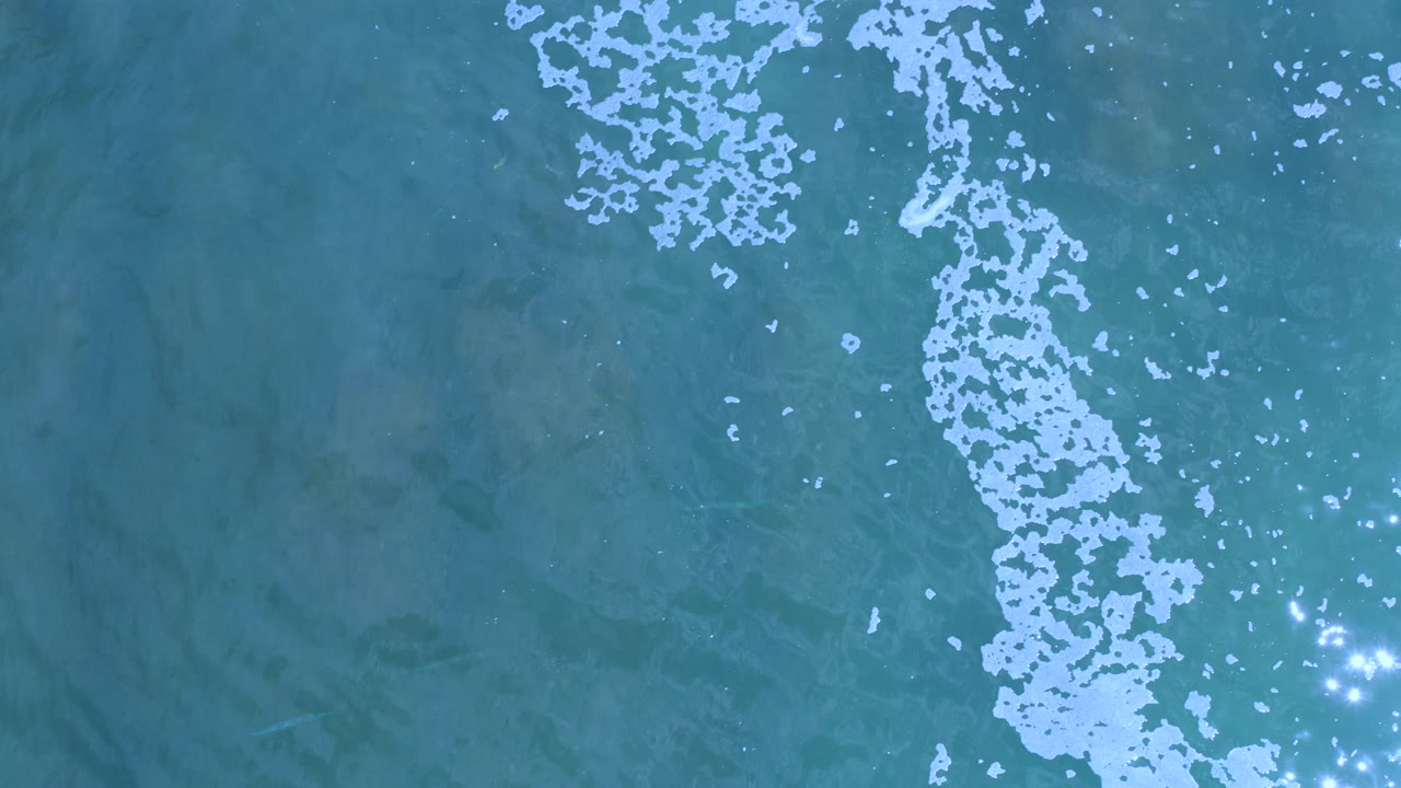 Overhead turquoise ocean with white bubbles and sun glints.