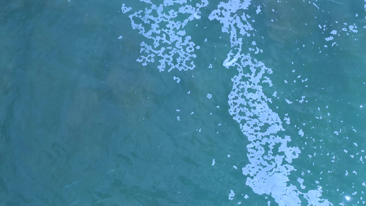 Aerial ocean surface with scattered foam and clear water.