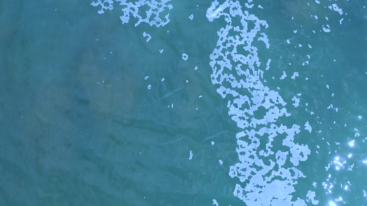 Ocean surface with white foam line and sparkling highlights.