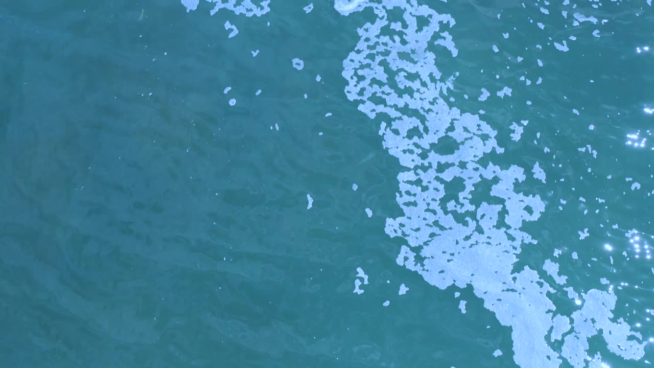 Aerial water surface with foam cluster and bright reflections