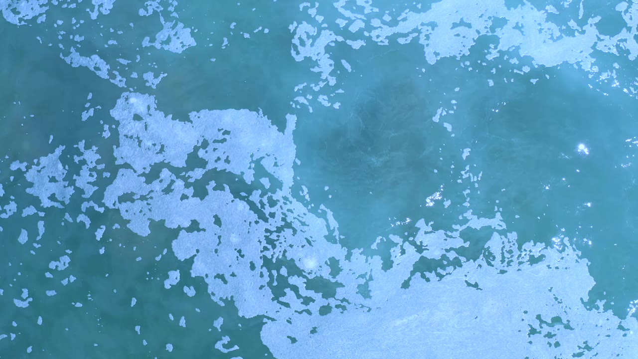 Overhead Los Cabos ocean frame with white foam clustered through the center and lower right, blue-green water around it, and no visible people.