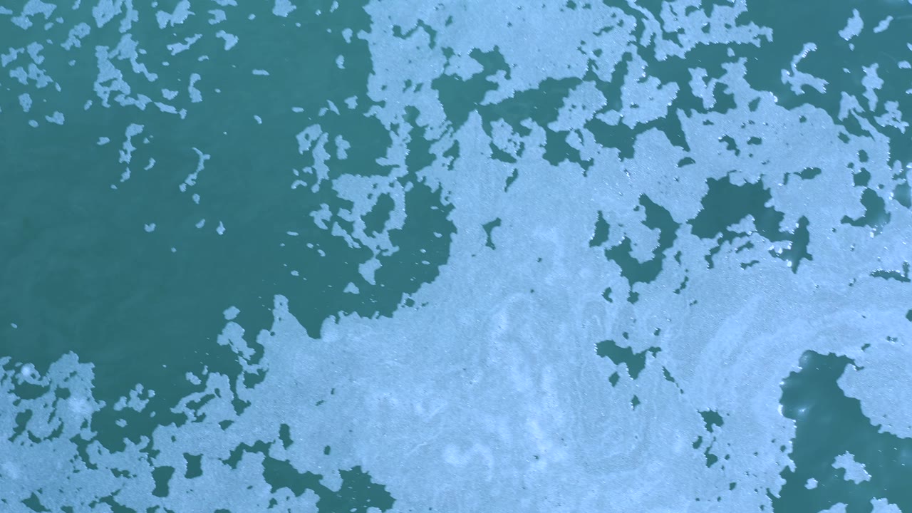 Top-down ocean surface with broad pale foam areas.
