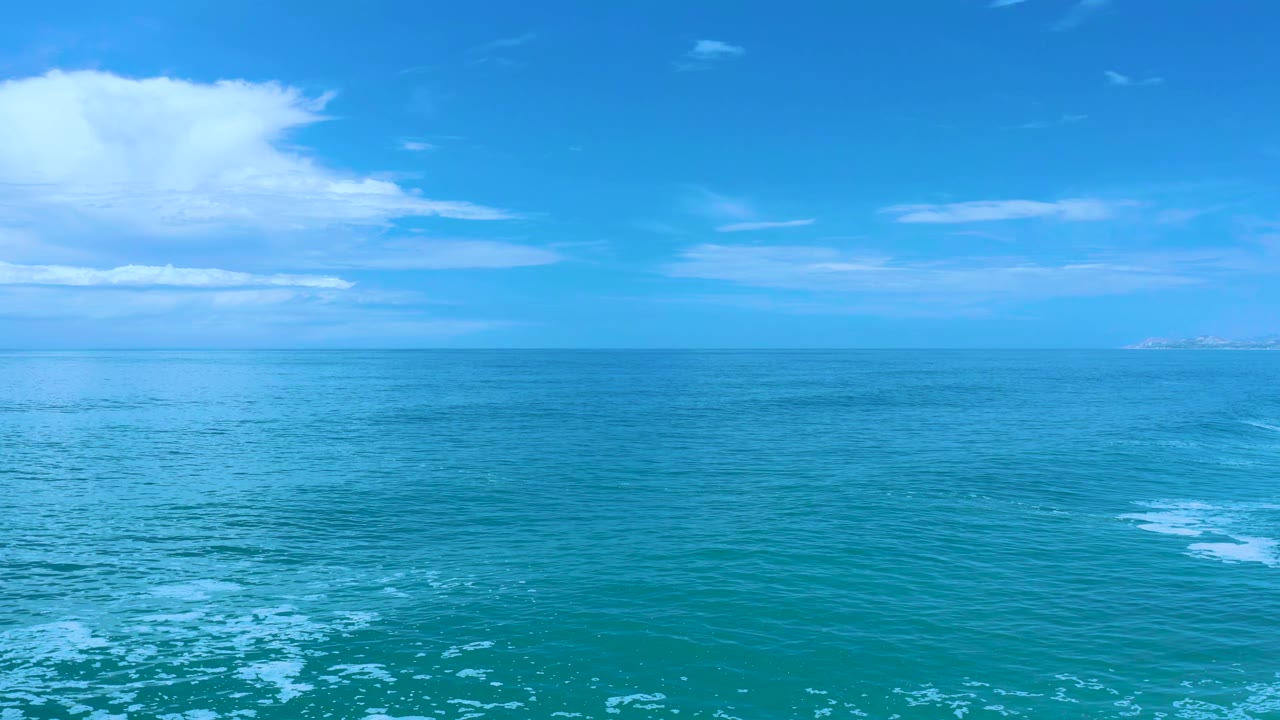 Los Cabos ocean view one second in, with a level horizon, pale cloud bands on the left, faint land on the right, and no visible people.