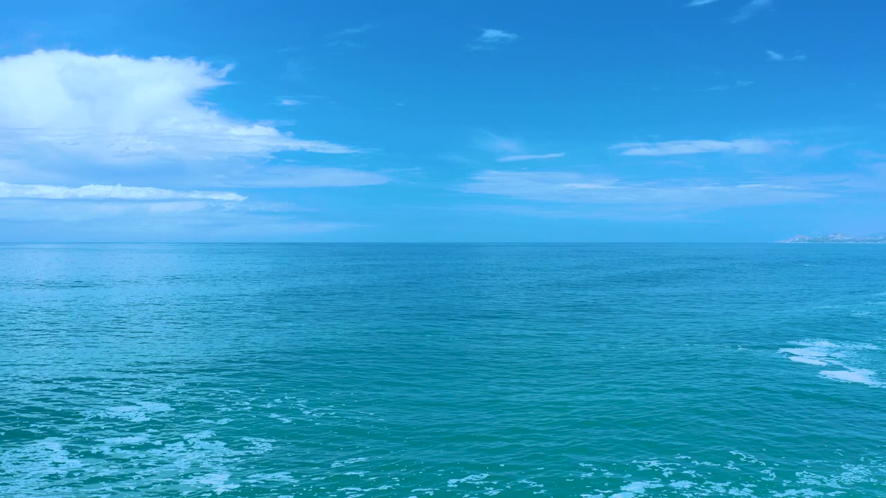 Mid-clip Los Cabos water view with low white clouds near the horizon, smooth blue sea across the frame, and no visible people.