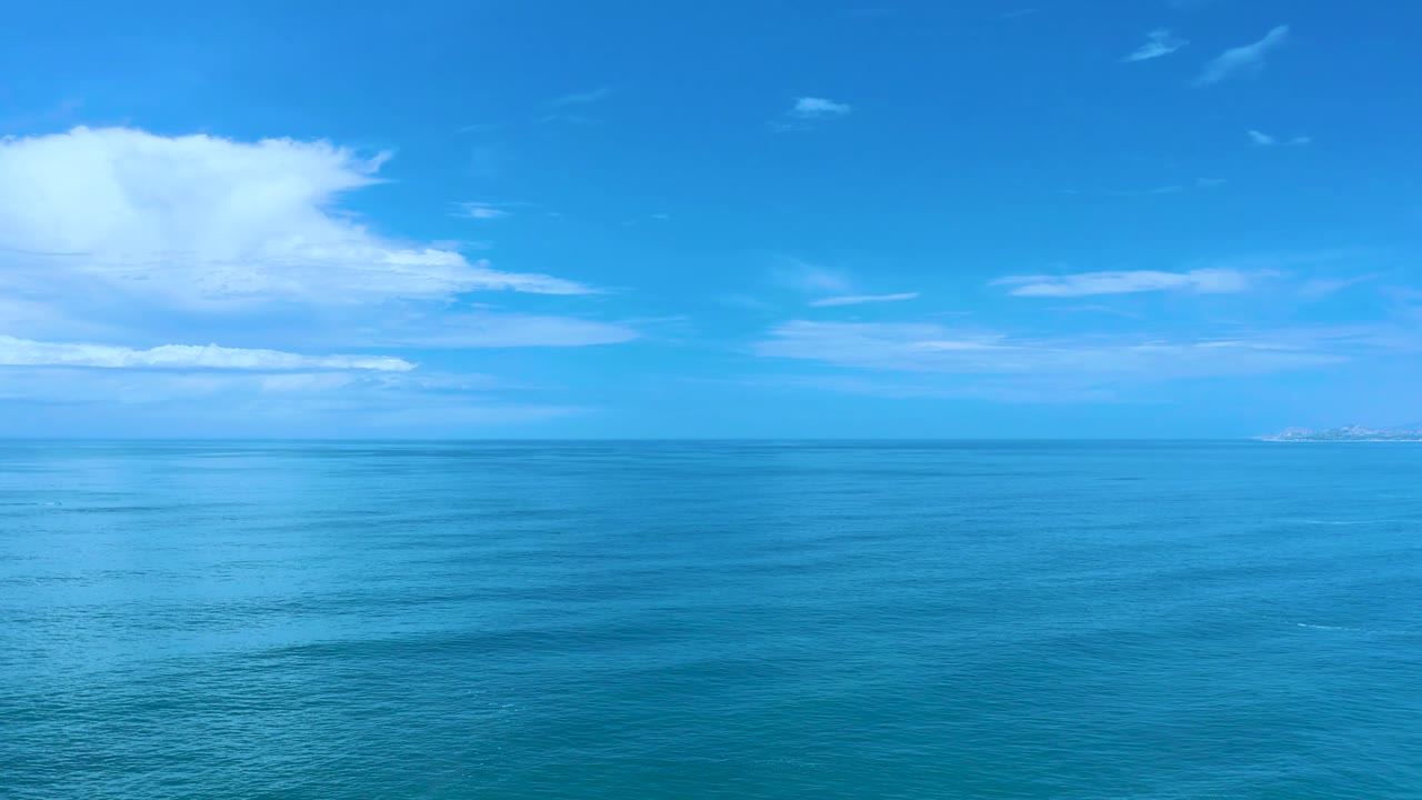 Los Cabos ocean horizon under saturated blue sky, with the large white cloud still left of frame and no visible people or boats.