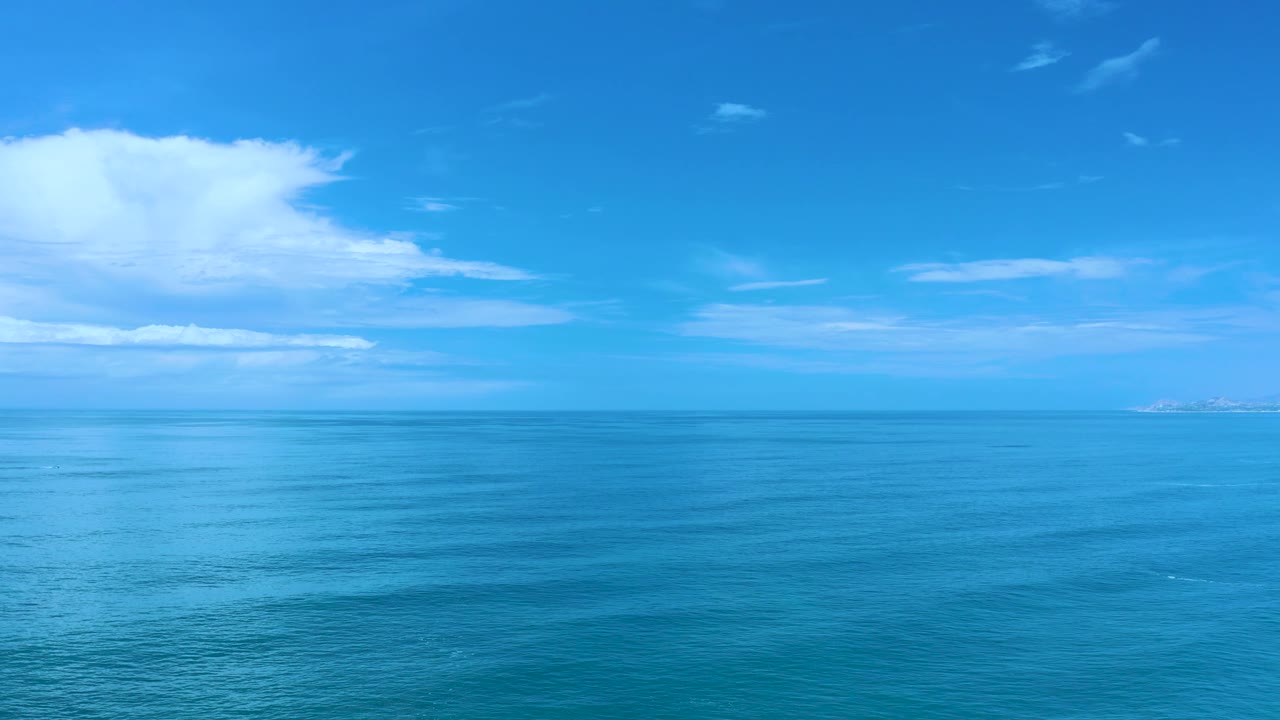 High wide view over the Los Cabos sea with calm surface bands, scattered clouds across the sky, a straight horizon, and no visible people.