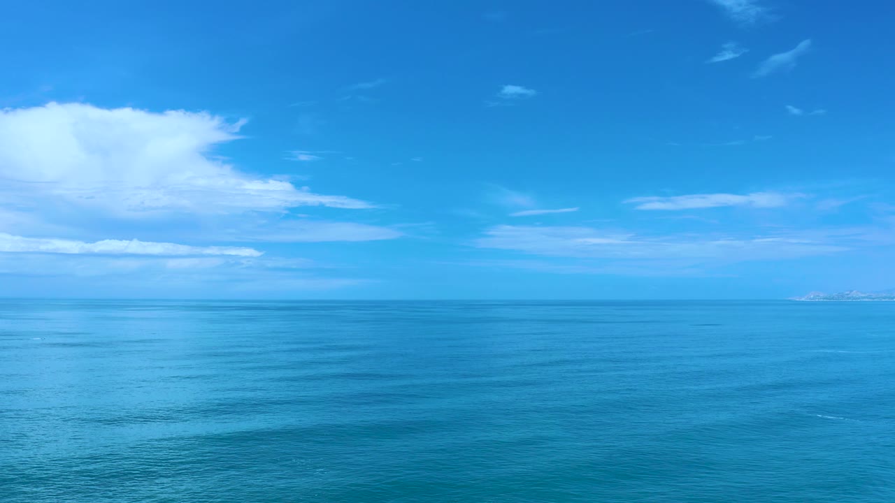 Los Cabos coastal water fills the lower frame while bright blue sky and a broad white cloud layer sit above the horizon, with no visible people.