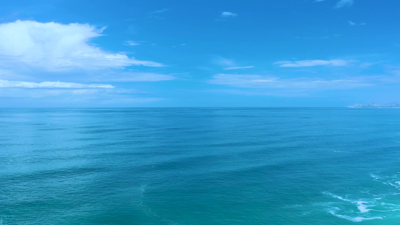 Los Cabos ocean frame with calm rippled water filling the foreground, thin cloud bands above the horizon, a distant landform at right, and no visible people.