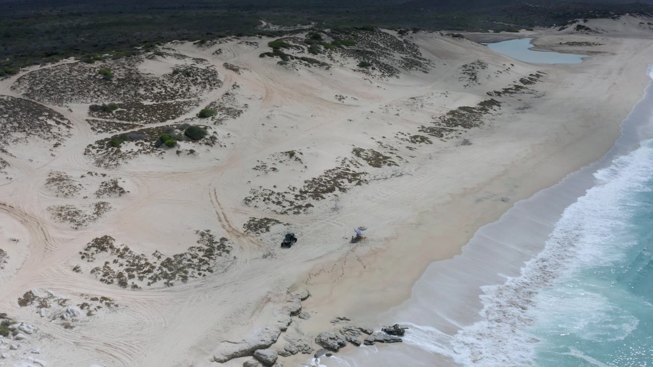 Aerial view of sandy dunes, rocky shore, and turquoise surf