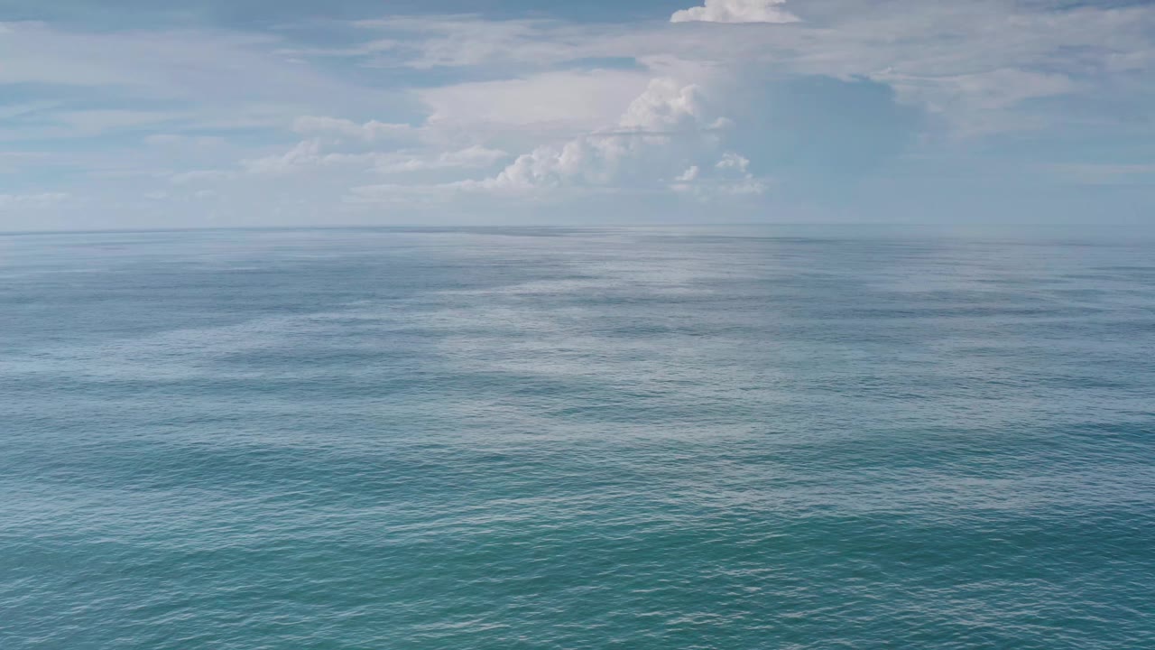 Los Cabos ocean view at one second, with textured blue water in the foreground, a thin distant horizon, cloud buildup on the left, and no visible people.