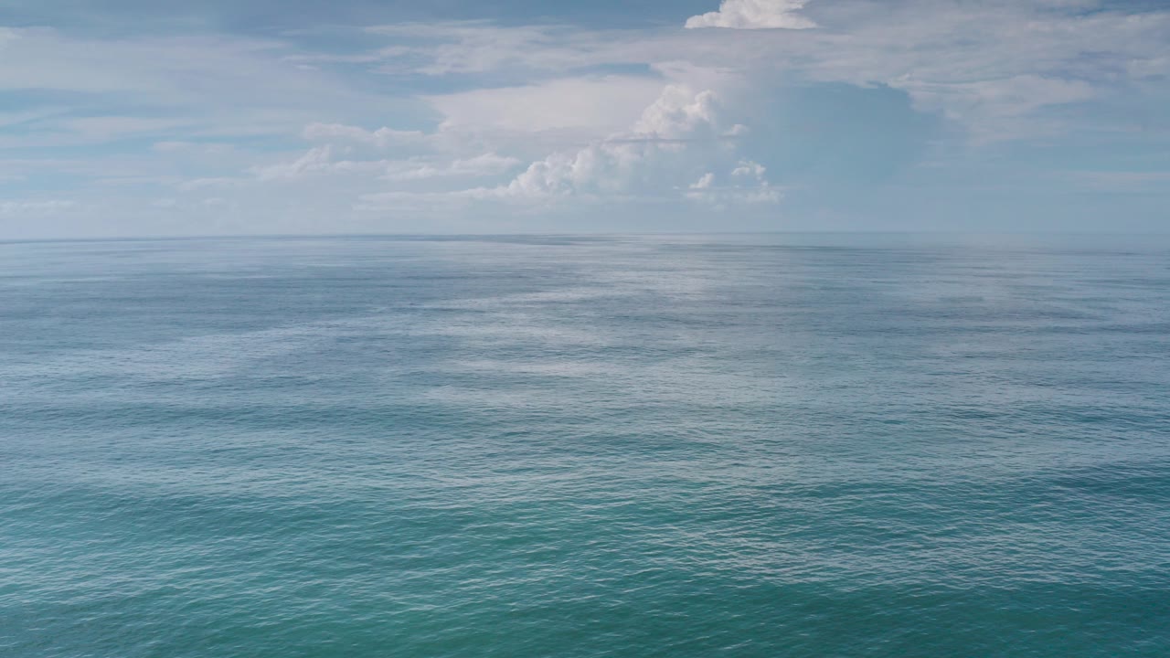 Wide Los Cabos ocean view at the start of the clip, with turquoise water below a level horizon, pale blue sky, distant white clouds, and no visible people.