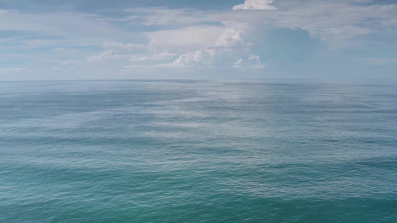 Turquoise sea surface and distant cloud bank under blue sky.
