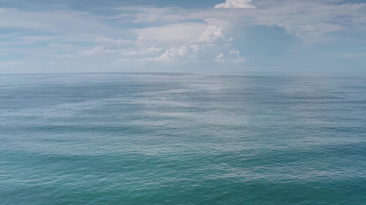 Wide Los Cabos sea view with darker blue water bands near the horizon, lighter turquoise foreground water, layered pale clouds, and no visible people.