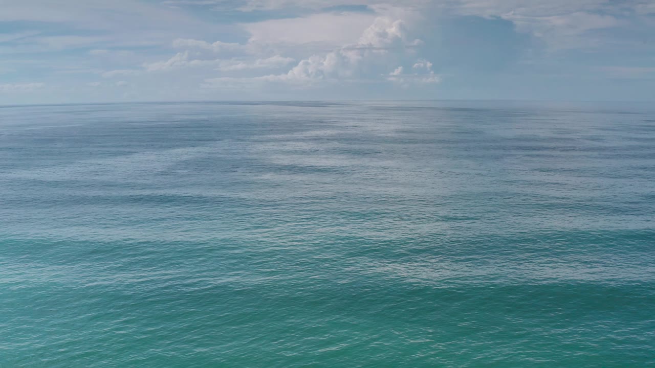 Open ocean fills the frame below small cloud patches over Los Cabos, Mexico, with subtle wave bands and no visible people.