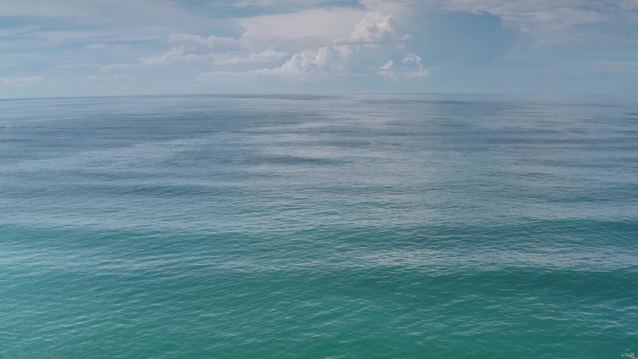 Calm turquoise water sits below a pale sky in Los Cabos, Mexico, with darker surface streaks near the horizon and no visible people.