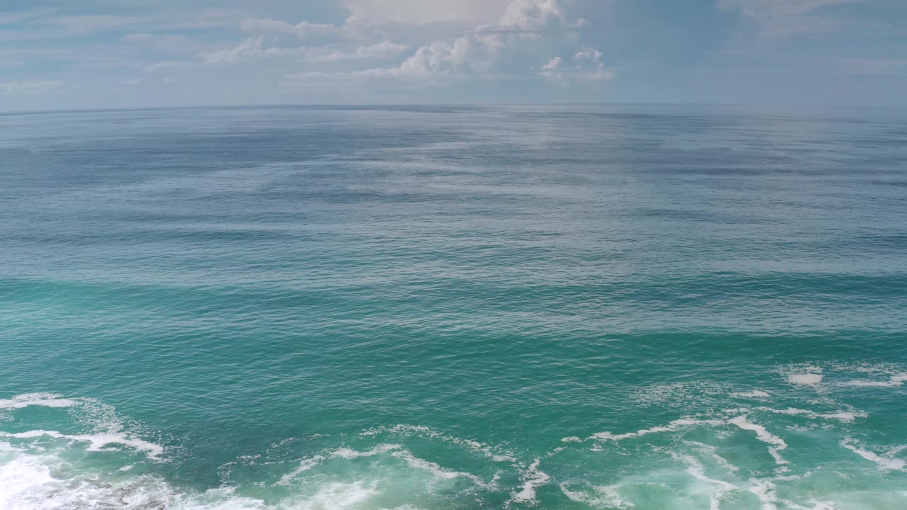 Los Cabos ocean surface shows small white foam patches across blue-green water, a level horizon, pale sky, and no visible people.