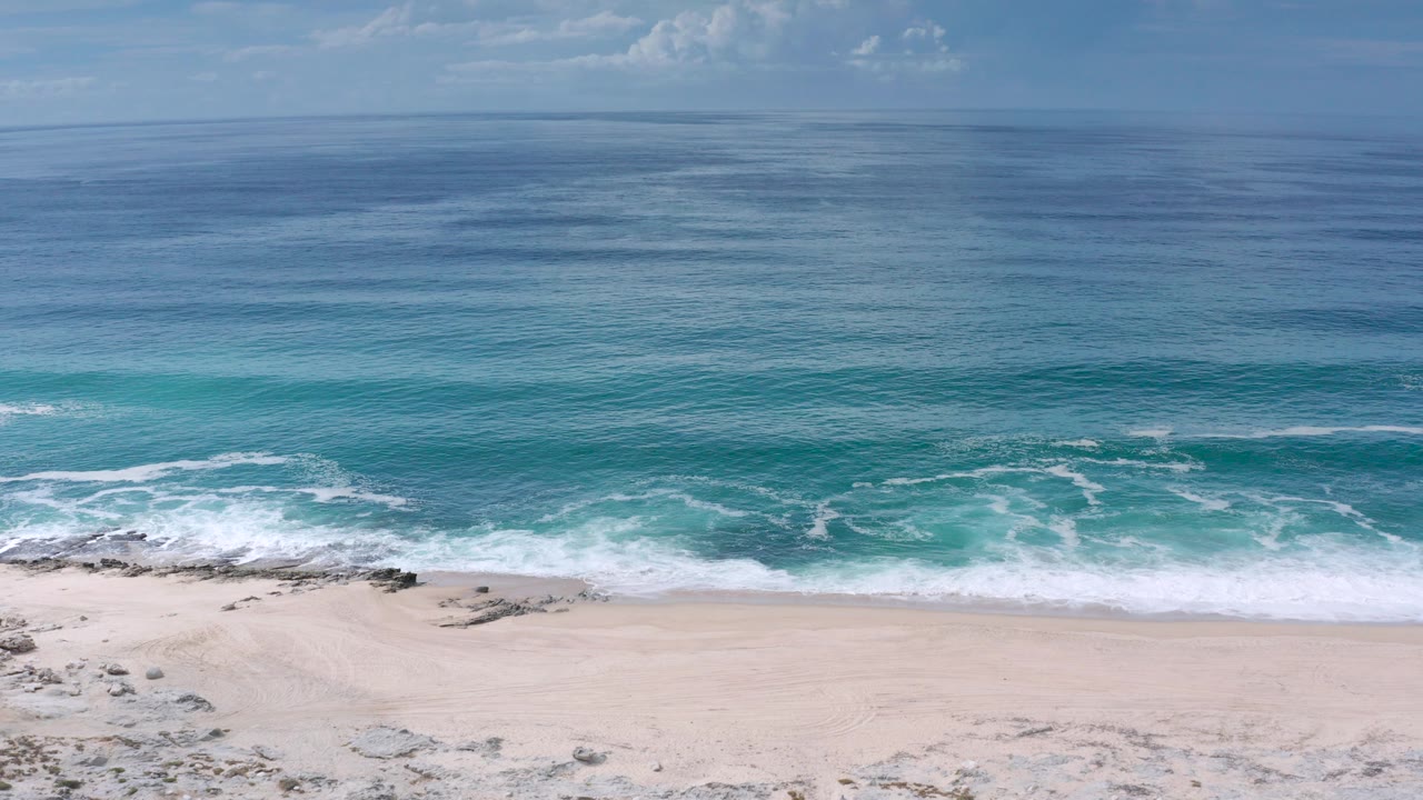 Aerial view of turquoise ocean surf meeting a pale sandy beach