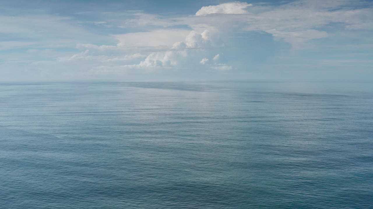 Open ocean under a pale blue sky with large white clouds.