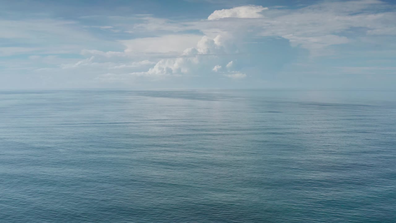 A calm Los Cabos ocean view shows faint surface texture, a distant horizon, and soft clouds occupying the upper frame with no visible people.