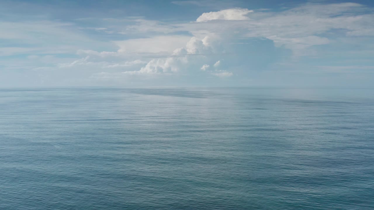 Los Cabos open water appears blue-green beneath a hazy horizon and bright white cloud banks, with no visible people, boats, or structures.