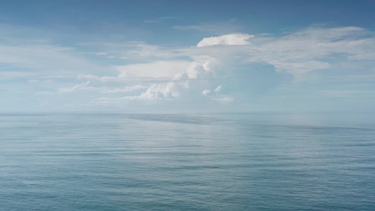 Los Cabos, Mexico ocean horizon with calm blue water in the foreground, pale sky above, a white cloud bank near the horizon, and no visible people.