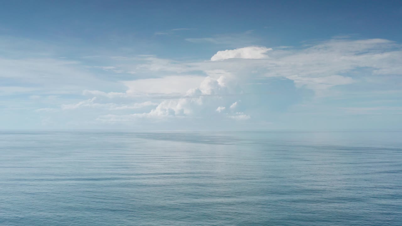 Opening frame of calm ocean water and a distant horizon under scattered white clouds in Los Cabos, Mexico, with no visible people.
