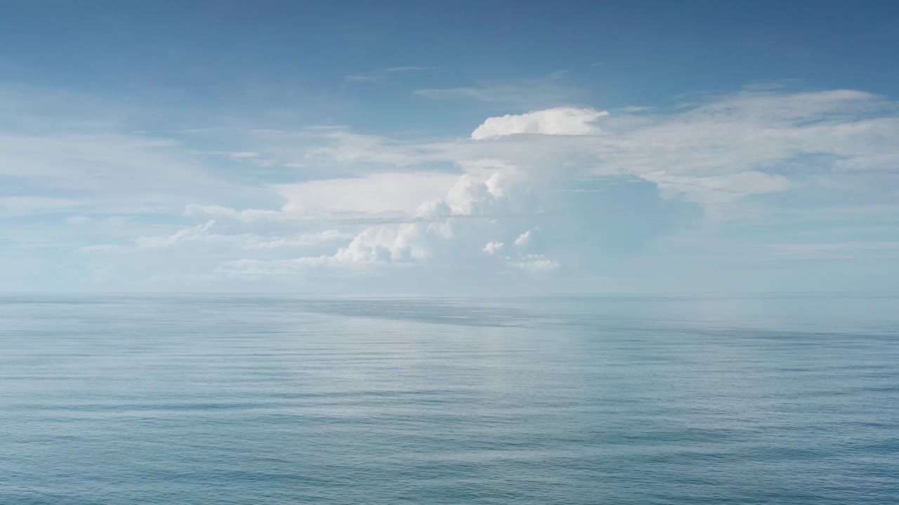 Aerial ocean view with subtle surface ripples, pale blue water, and soft cloud cover near the horizon in Los Cabos, Mexico, with no visible people.