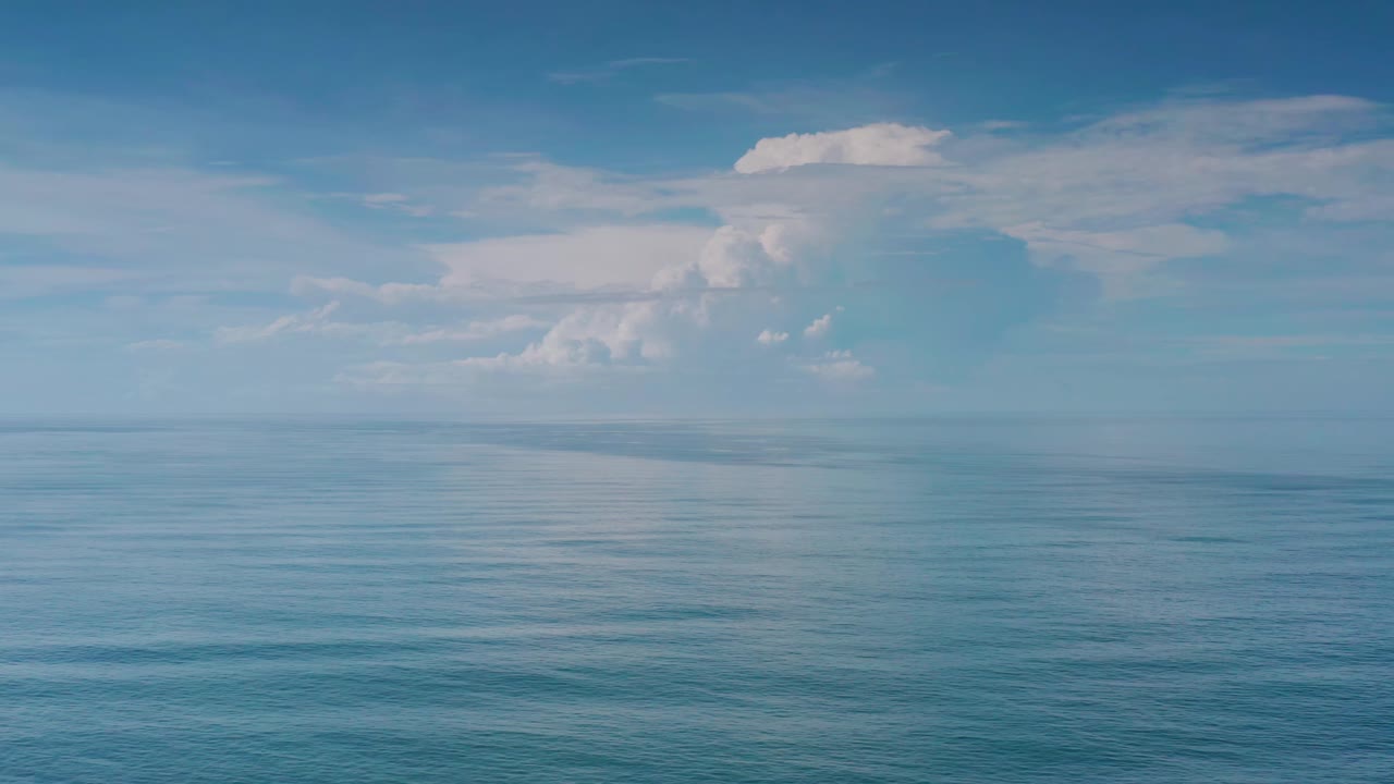 Calm ocean surface with distant horizon and layered white clouds.