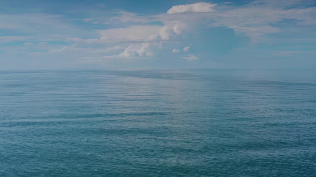 Mid-clip Los Cabos ocean frame with calm blue water, a straight horizon, pale sky, and soft white clouds, with no visible people.