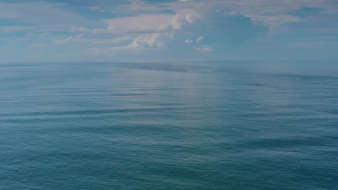 Opening frame of the Los Cabos ocean with calm blue water below a distant horizon, pale clouds above, and no visible people.