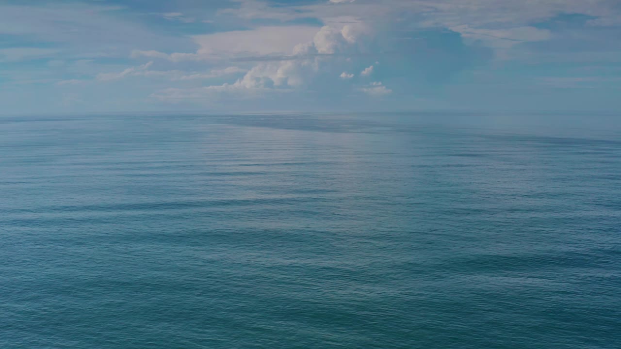 Los Cabos sea surface stretches toward a level horizon, with soft cloud shapes across the upper sky and no visible people.
