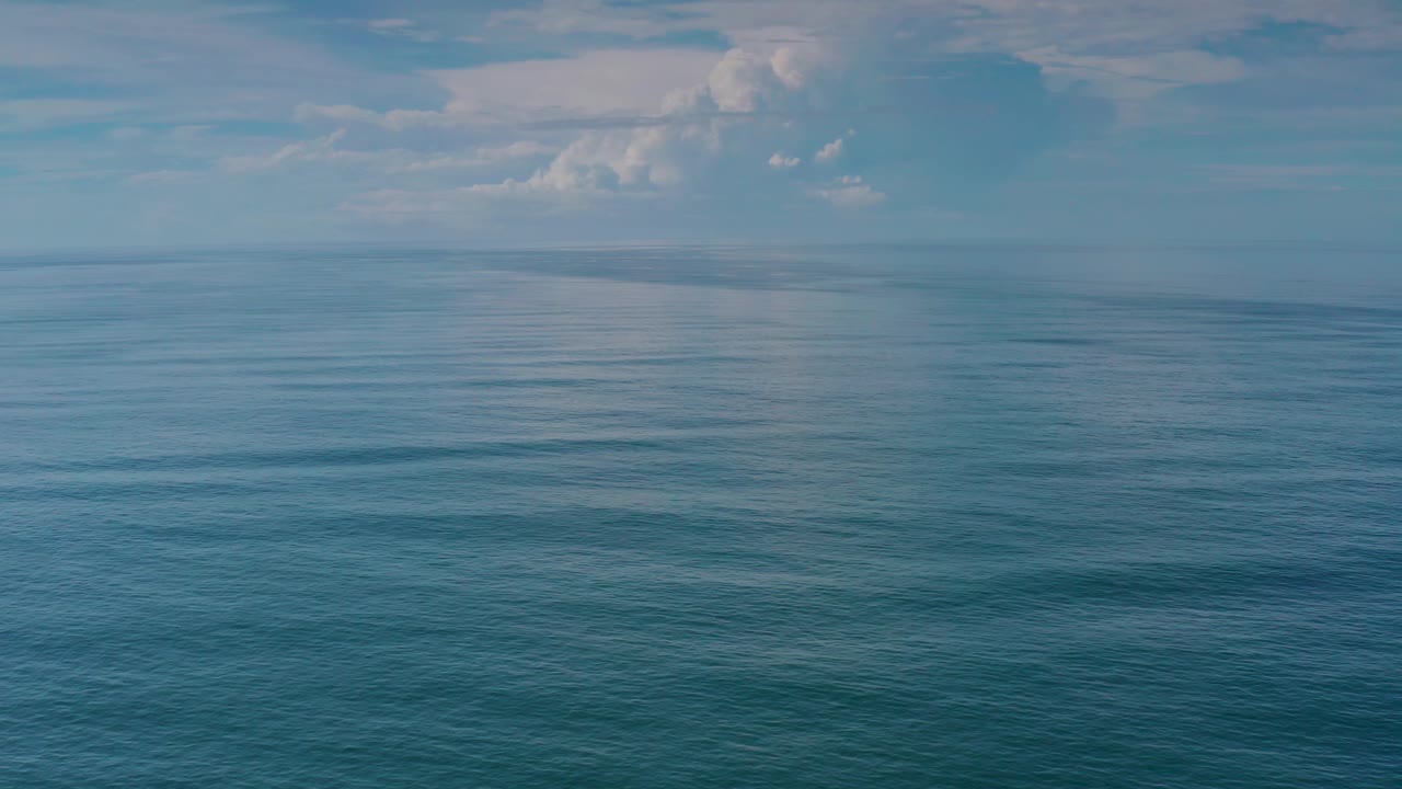 The frame shows blue ocean ripples in the foreground, a faint far horizon, hazy sky, and no visible people in the Los Cabos coastal view.