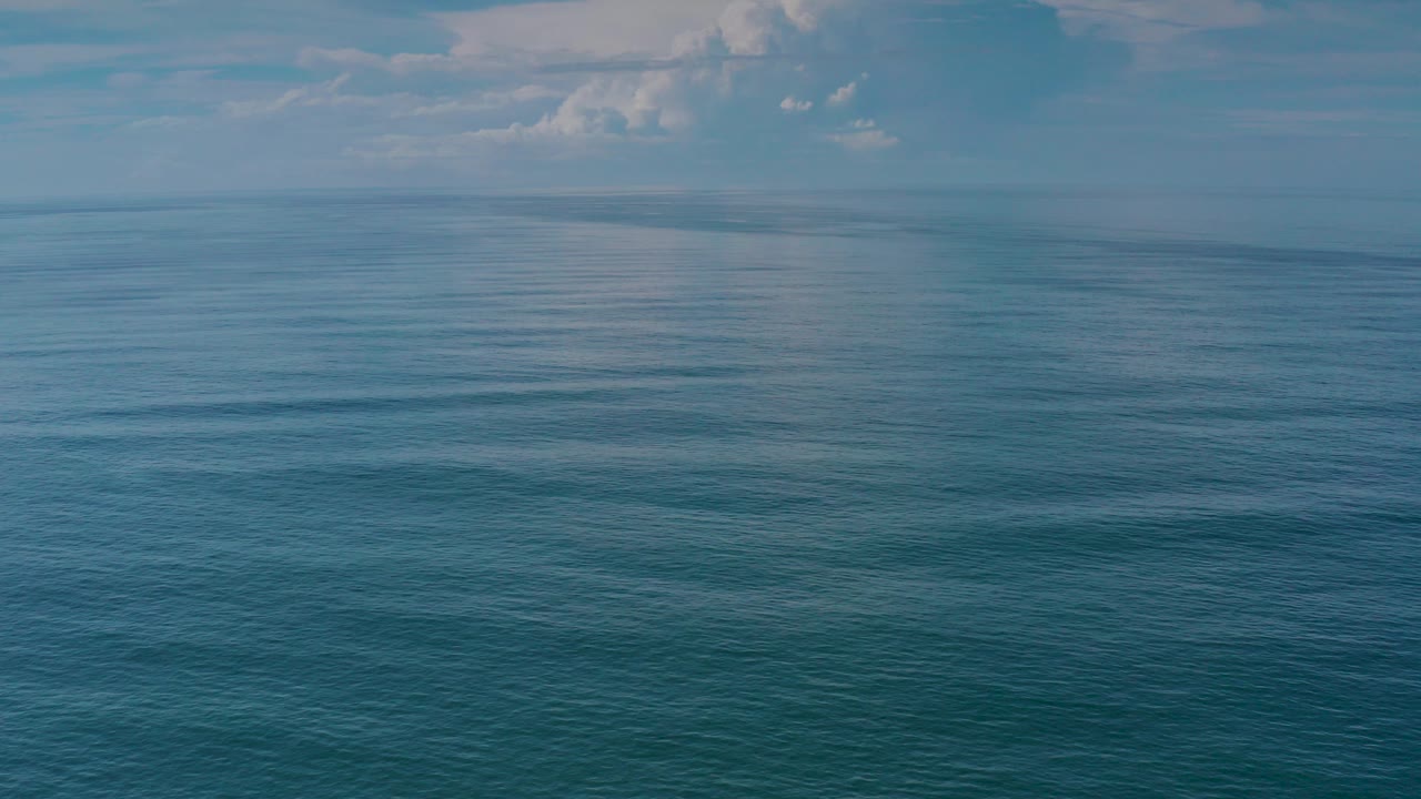 Opening frame of calm blue ocean in Los Cabos, Mexico, with a level horizon, soft cloud cover near the top edge, and no visible people.