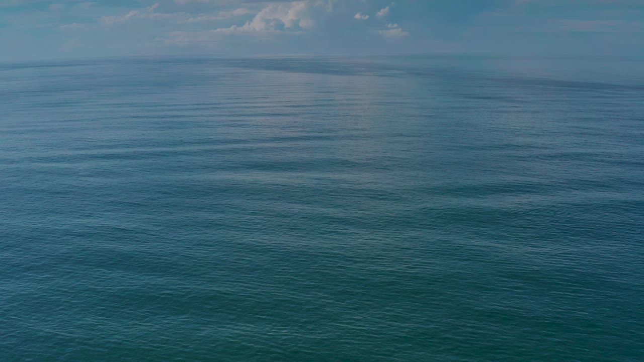 Blue ocean surface stretches toward a thin cloudy horizon in Los Cabos, Mexico, with subtle wave texture and no visible people.