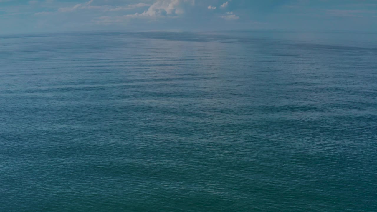 Open sea fills the frame in Los Cabos, Mexico, with muted teal water, a level horizon, soft cloud patches, and no visible people.
