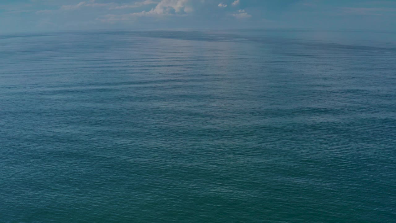 A wide Los Cabos ocean view shows blue-green water below a pale cloudy sky, with fine ripples across the surface and no visible people.