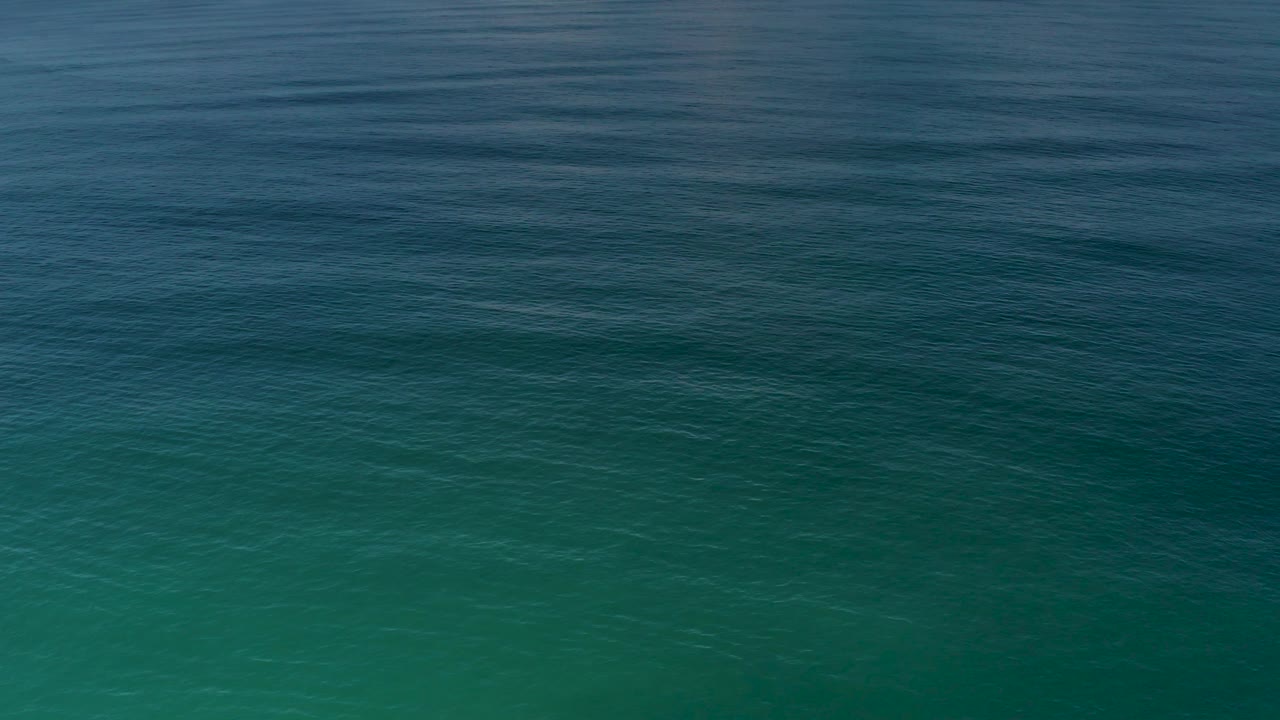 Darker blue ripples cross the upper part of the Los Cabos ocean frame while greener aquamarine water sits below, with no visible people.