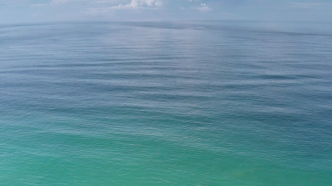 Early frame of Los Cabos ocean water showing a broad turquoise foreground, darker rippled midwater, pale sky, and no visible people.