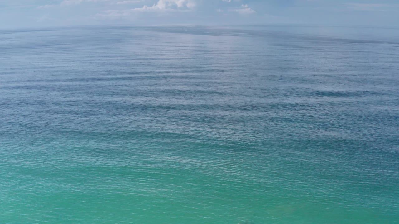Los Cabos ocean surface with layered turquoise water in front, smooth darker blue water toward the horizon, soft cloud detail, and no visible people.