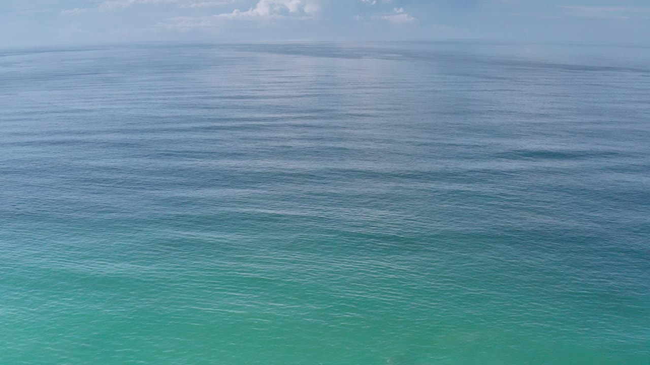 Mid-clip frame of calm Los Cabos sea water, with horizontal ripple bands, muted blue distance, pale sky, and no visible people.
