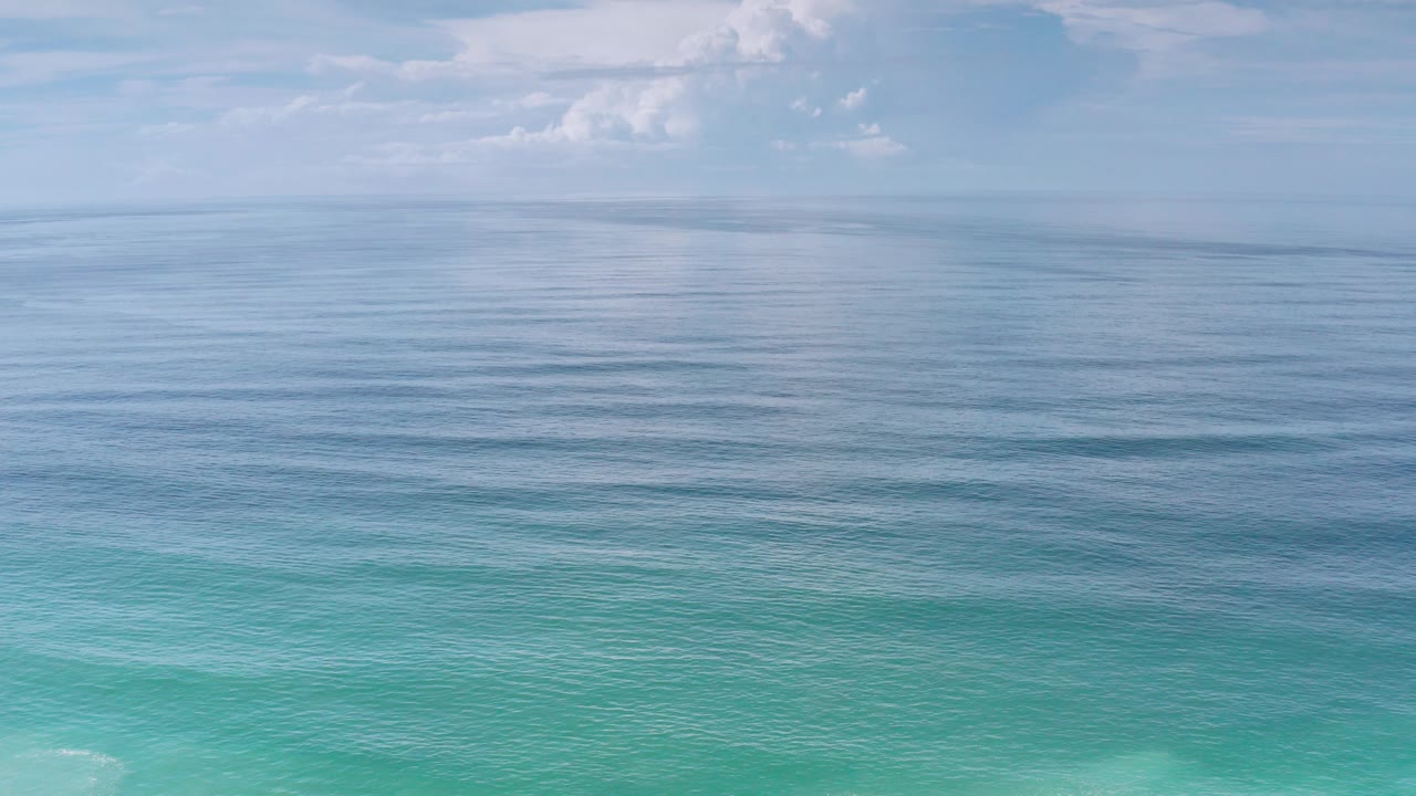 Opening frame of Los Cabos ocean water, with turquoise shallows at the bottom, darker ripples toward the horizon, pale clouds above, and no visible people.