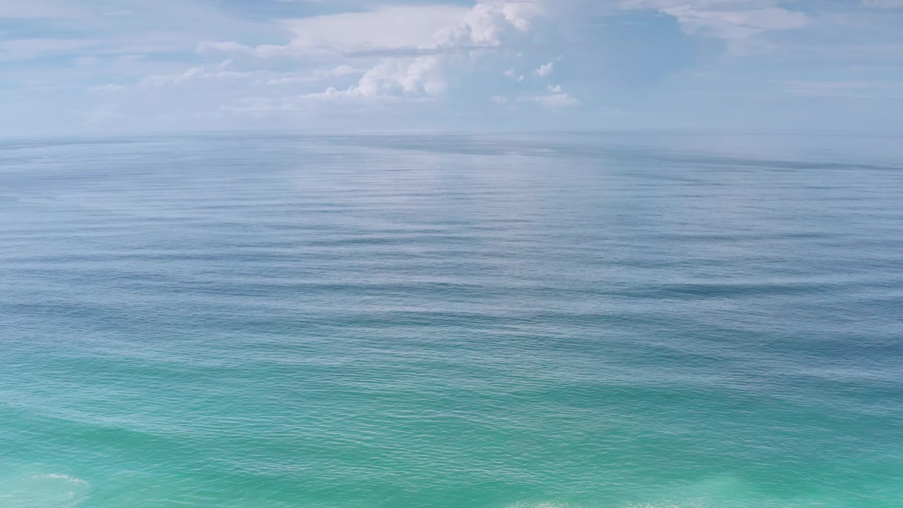 Third frame holds on Los Cabos coastal water, where light turquoise foreground tones shift into blue ripples beneath a soft cloud bank, with no visible people.