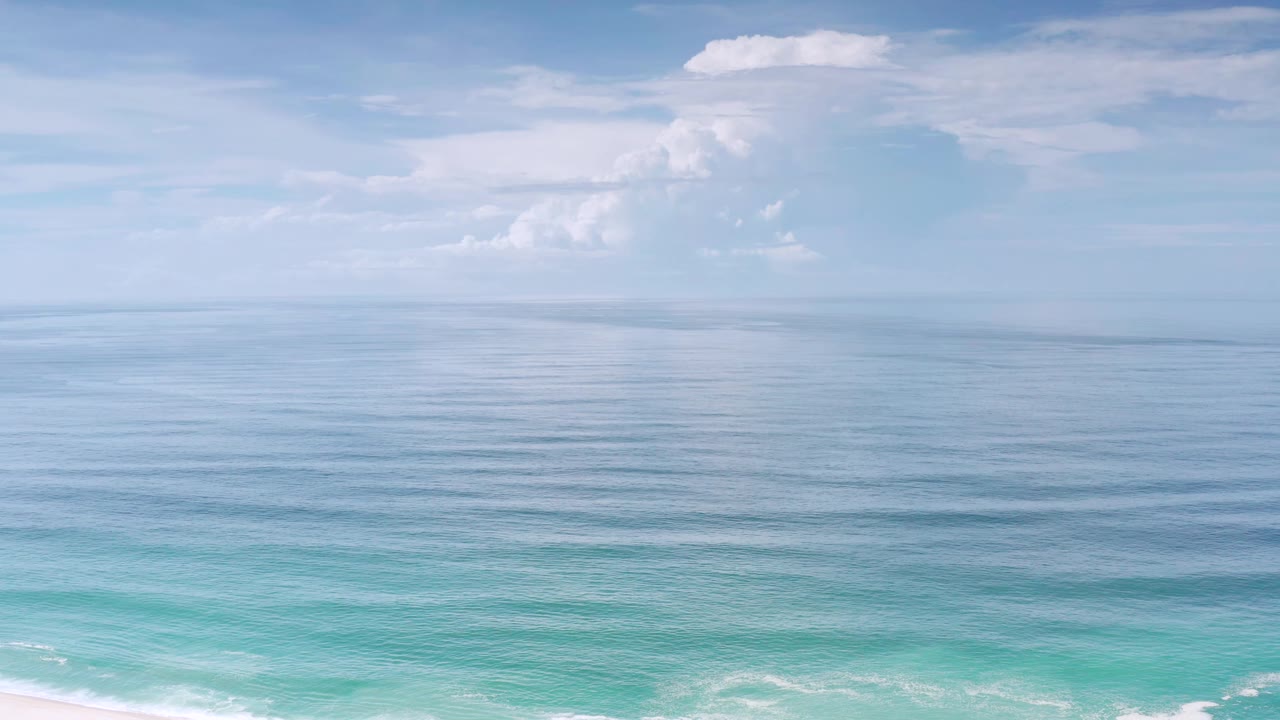 Los Cabos, Mexico ocean view with the horizon centered, a large white cloud mass left of center, light blue water bands, and no visible people.
