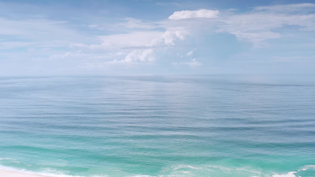 Los Cabos, Mexico coastal frame with layered blue sea, soft white clouds across the upper sky, faint surf along the lower edge, and no visible people.