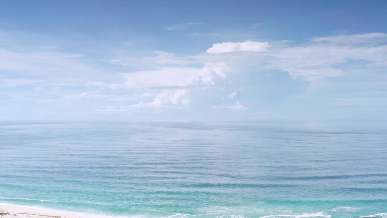 Los Cabos coastal water fills the frame beneath large white cloud banks, with the beach edge faintly visible and no visible people.